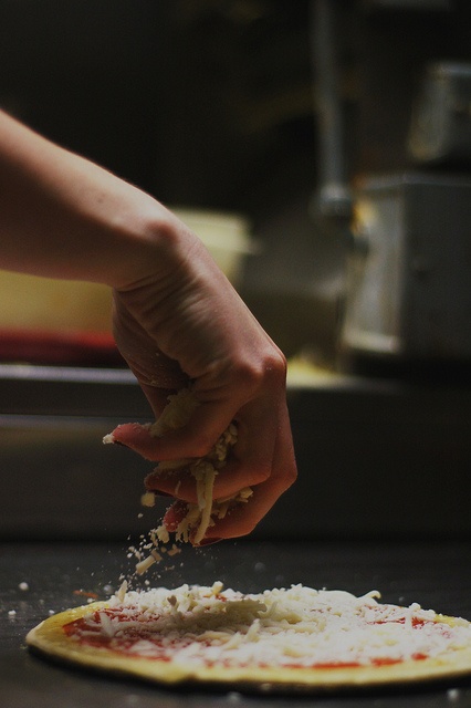 a person is sprinkling cheese on top of a pizza crust in a kitchen