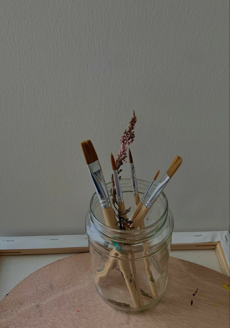 a jar filled with lots of brushes sitting on top of a wooden table