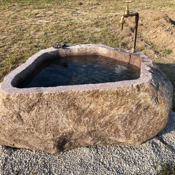 an outdoor hot tub in the middle of a field with grass and rocks around it