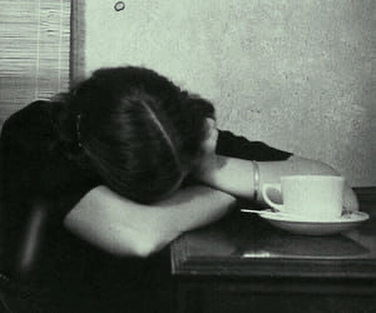 a black and white photo of a woman sitting at a table with her head down