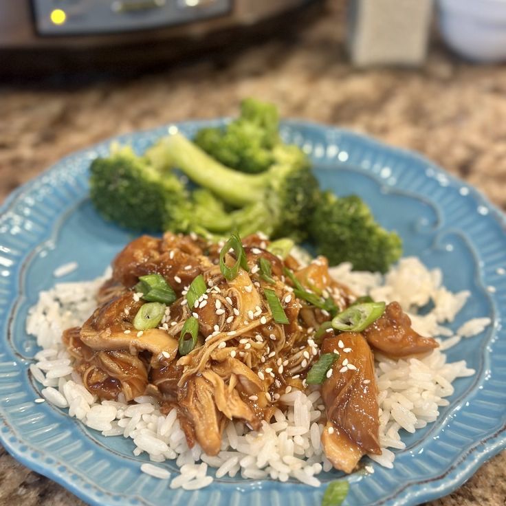 a blue plate topped with rice and meat next to broccoli on a counter