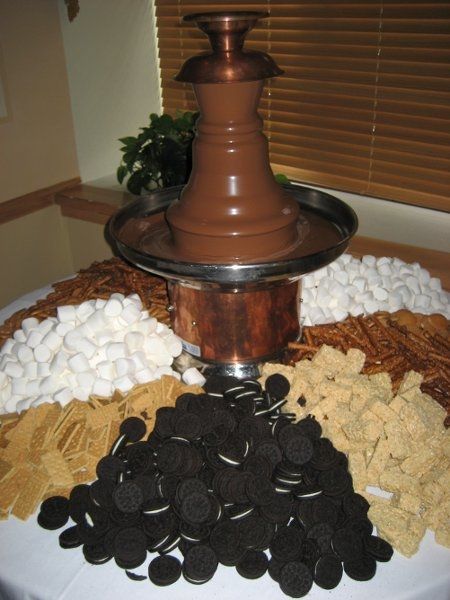 a table topped with a chocolate fountain and lots of cookies on it's side