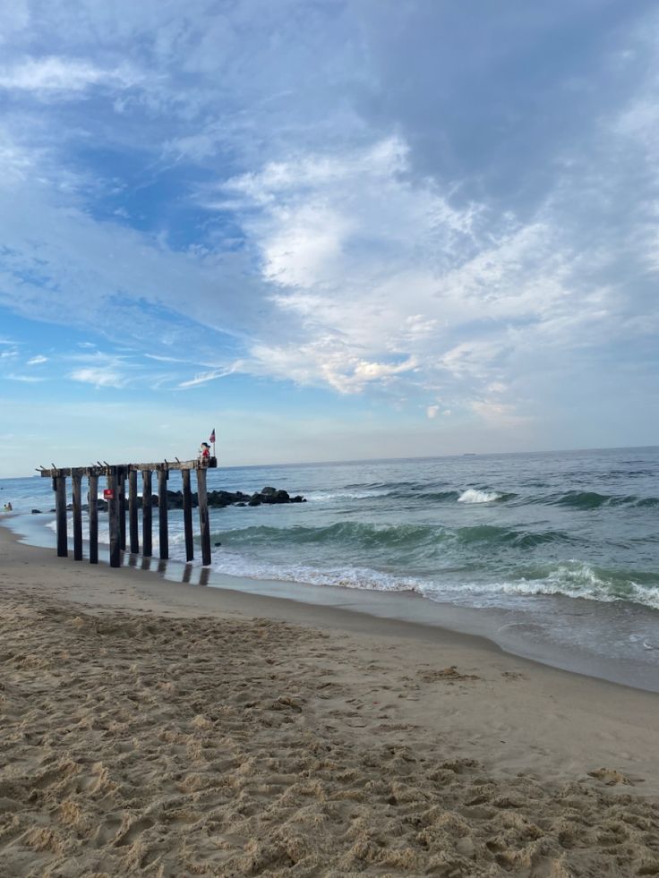 people are standing at the end of a pier on the beach next to the ocean