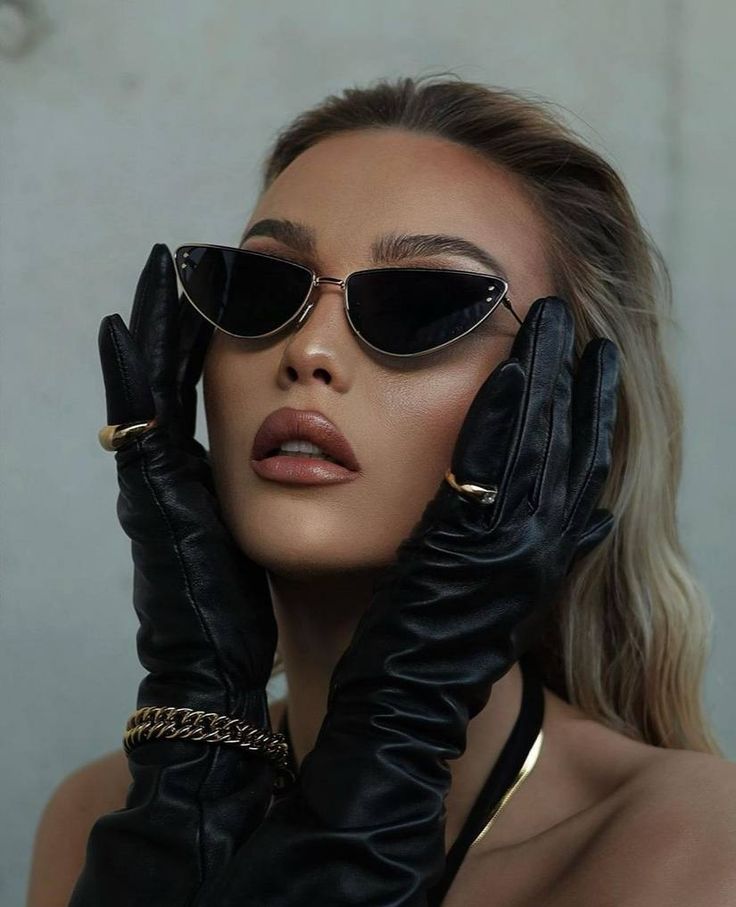 a woman wearing black gloves and holding her hands up to her face with sunglasses on