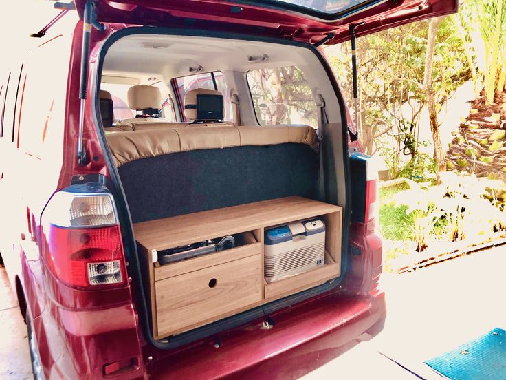 an open trunk in the back of a red van with its door open and shelves on it