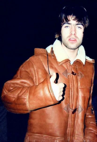 a man wearing a brown leather jacket giving the thumbs up sign with his right hand