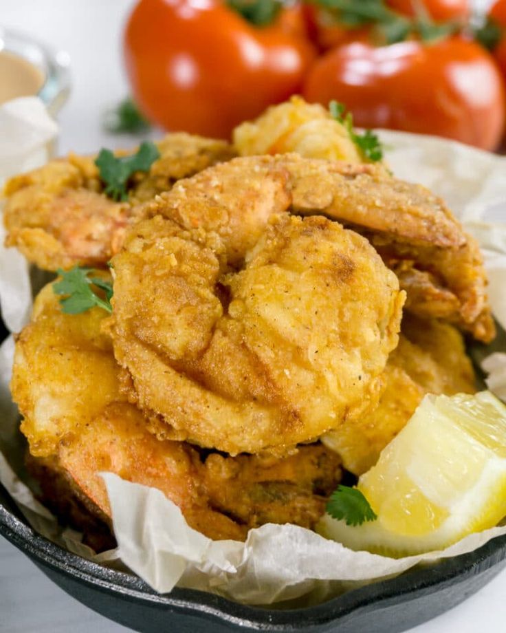 fried food in a frying pan with lemon wedges and tomatoes