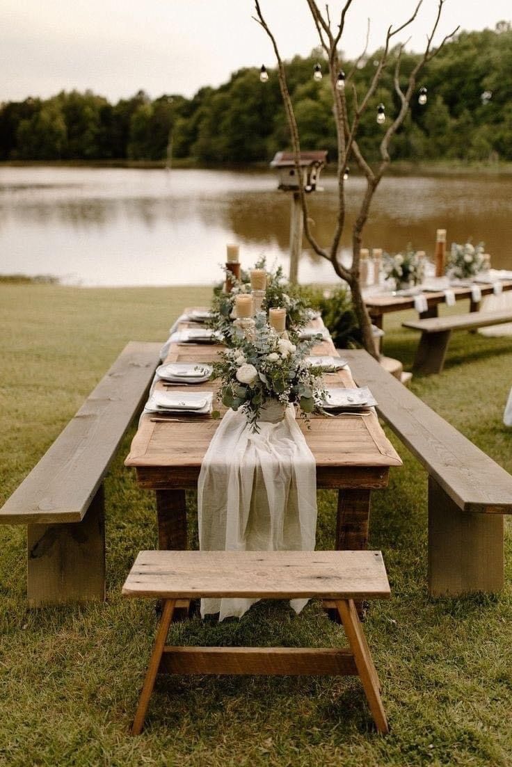 an outdoor table set up with flowers and greenery for a wedding reception by the water