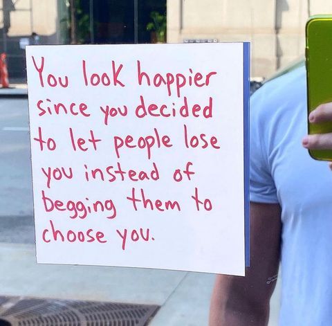 a person holding a cell phone in front of a sign that says you look happy since you decided to let people lose you instead of begging them to choose you