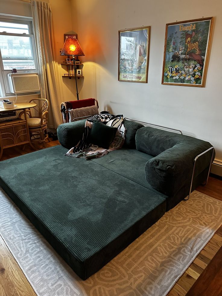 a living room with a large green couch on the floor and pictures hanging above it