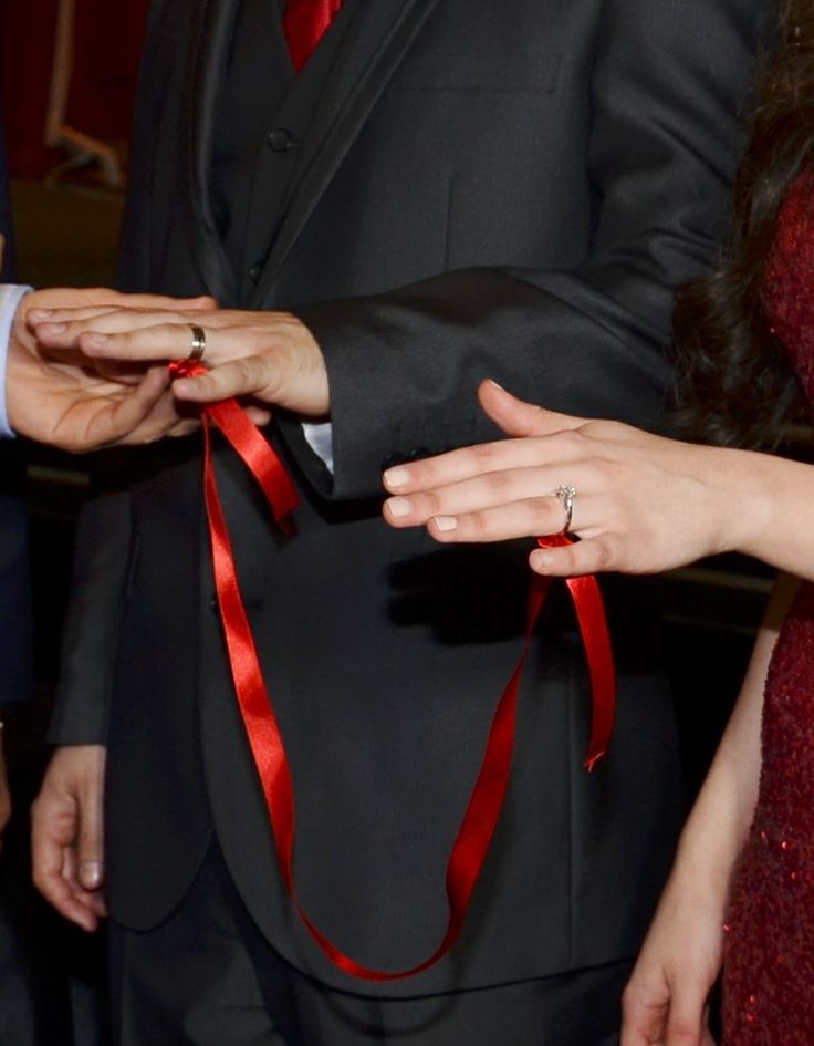 two people wearing red ties and black suits are holding hands with each other as they hold their wedding rings