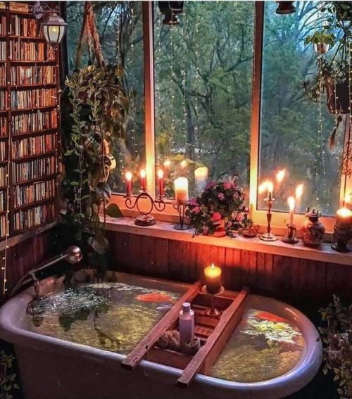 a bathtub filled with water surrounded by plants and candles in front of a window