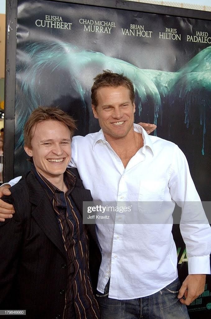 two men standing next to each other in front of a movie poster