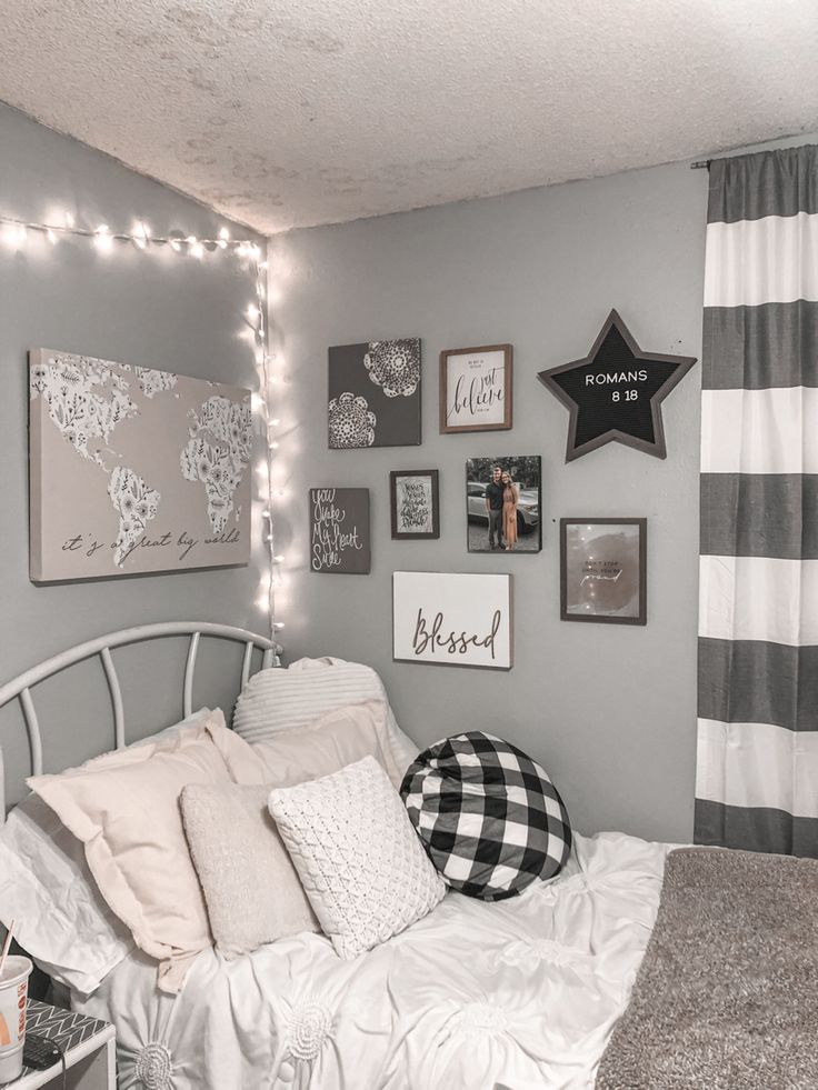 a bedroom decorated in gray and white with pictures on the wall, lights strung up above the bed