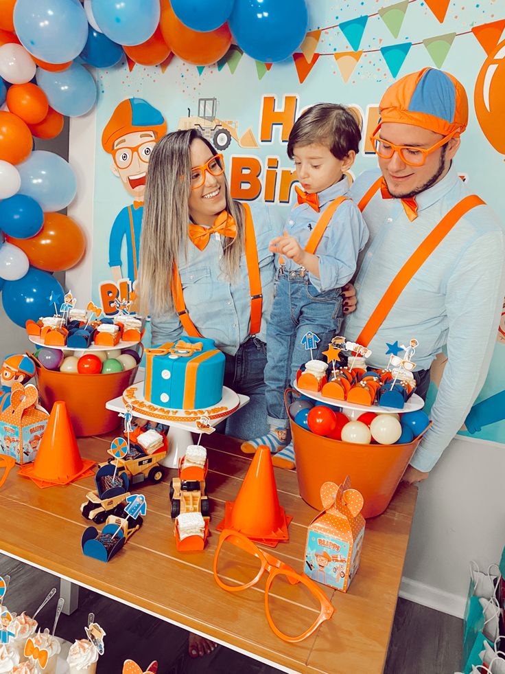 two children and an adult standing in front of a table with orange and blue decorations