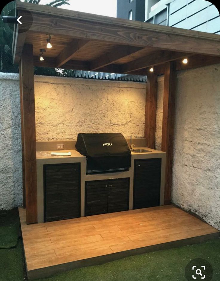 an outdoor bbq with grill, sink and cabinets under a pergolated roof