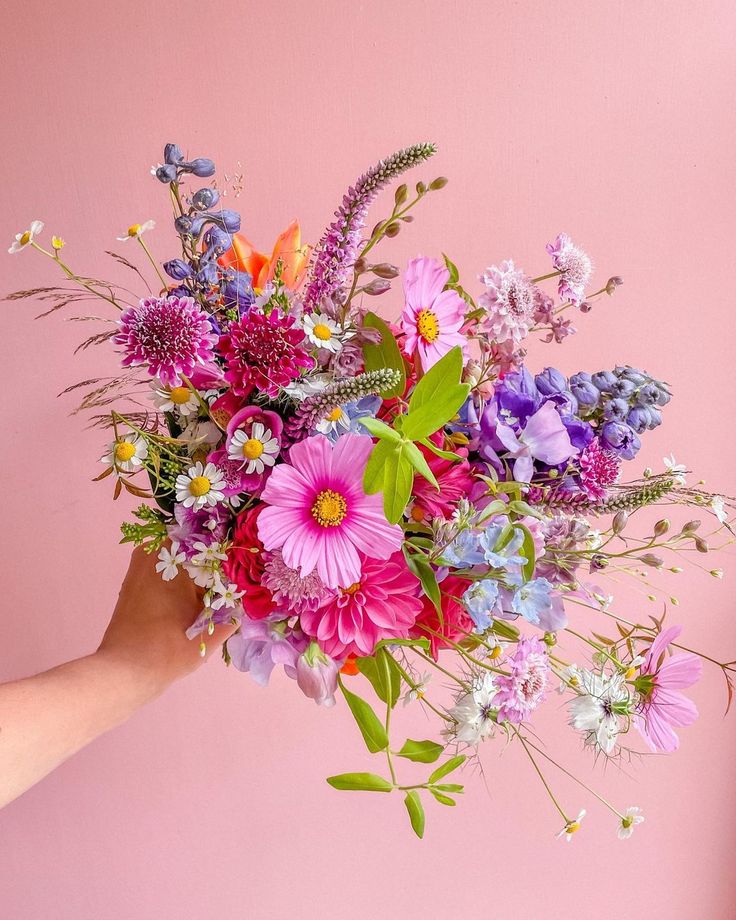 a person holding a bouquet of flowers against a pink background