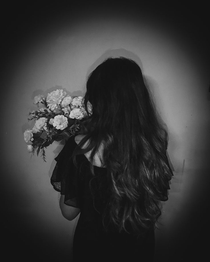 a woman with long hair holding flowers in front of her face and looking at the wall