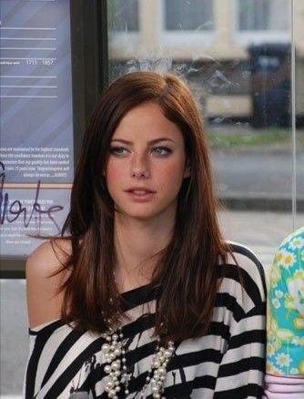 a woman sitting on a bench in front of a sign and wearing a striped shirt