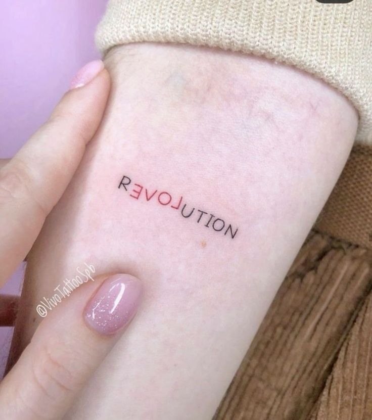 a woman's arm with the word revolution tattooed on her left forearm and pink nail polish