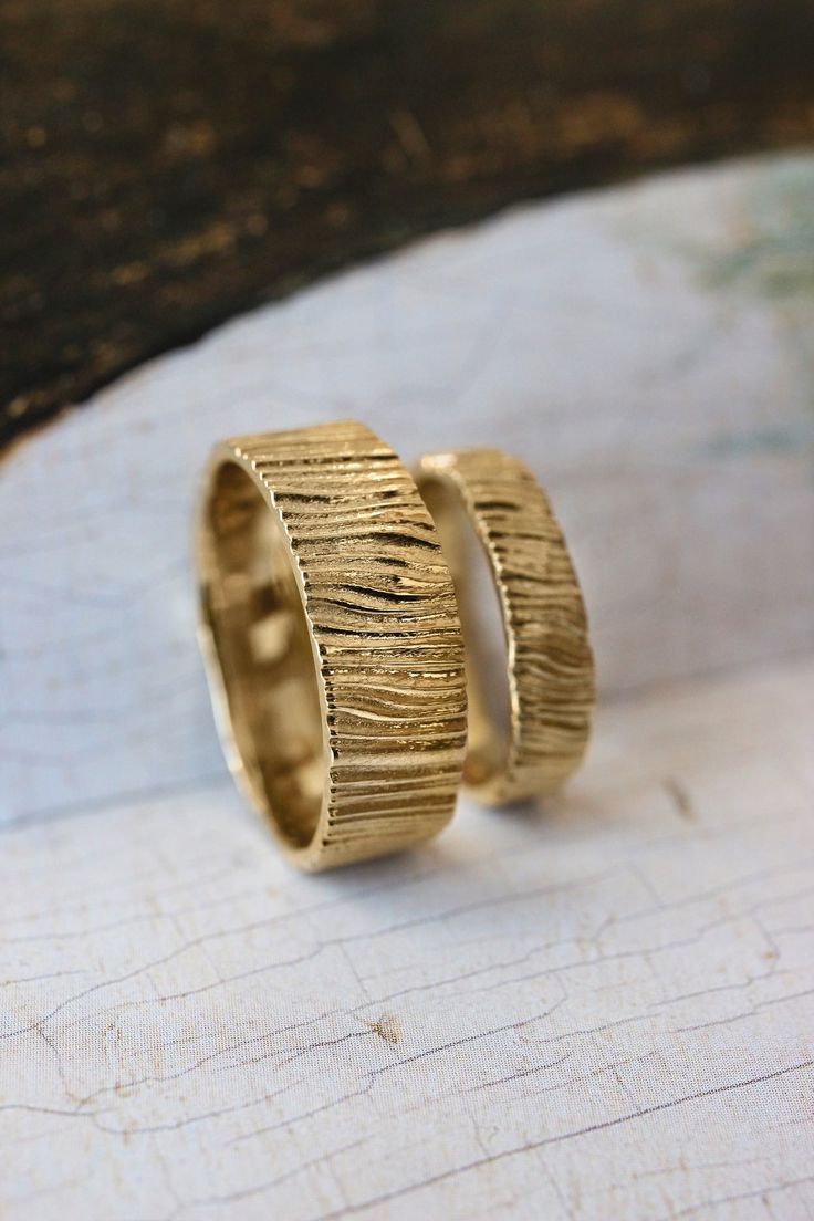 two gold rings sitting on top of a piece of wood