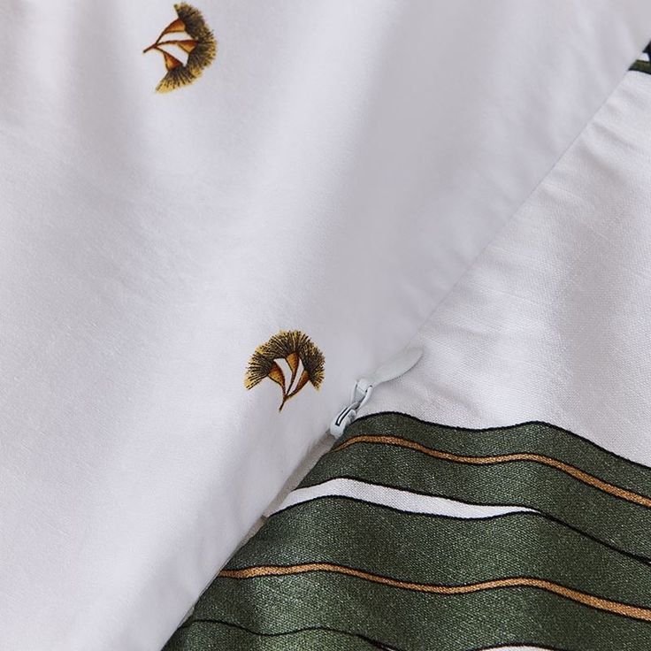 two pieces of white fabric with green and gold designs on them, one is folded to the side