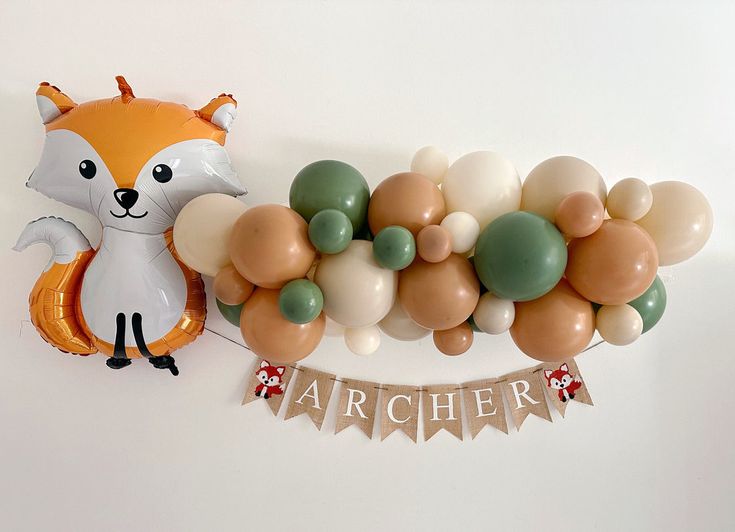 a balloon garland with an animal, fox and raccoon on the top is attached to a wall