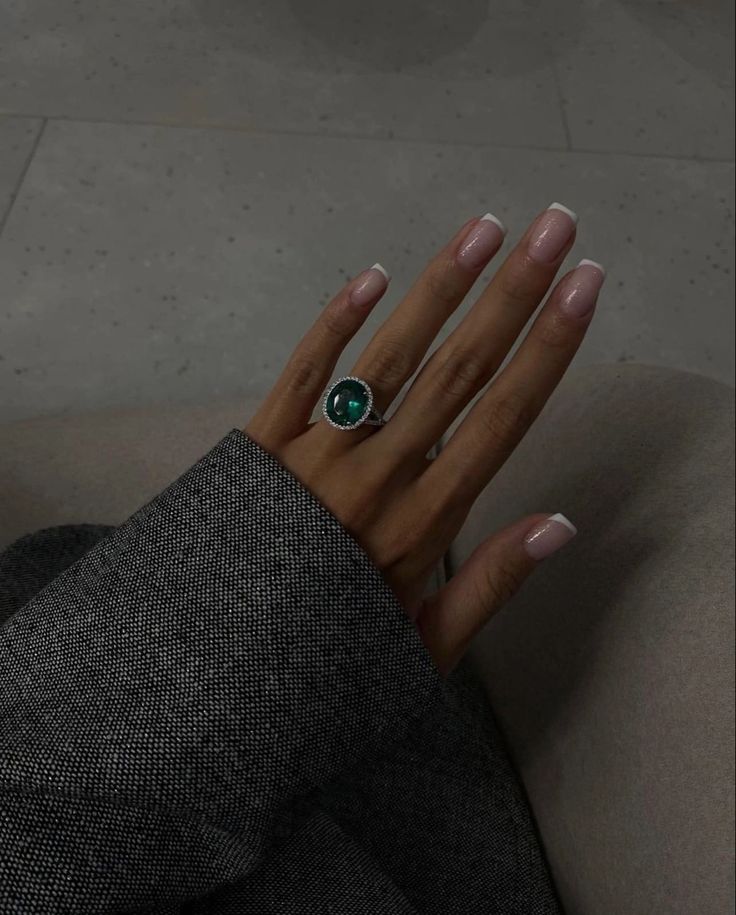 a woman's hand wearing a ring with an oval green stone on the middle