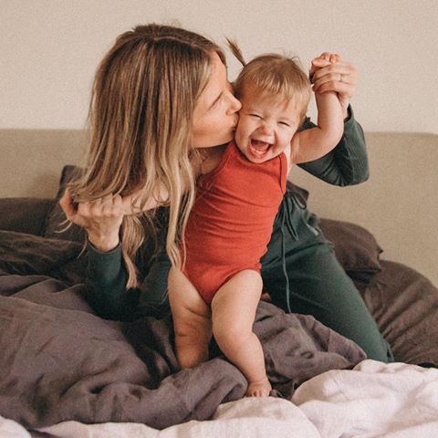 a woman kissing a baby on top of a bed