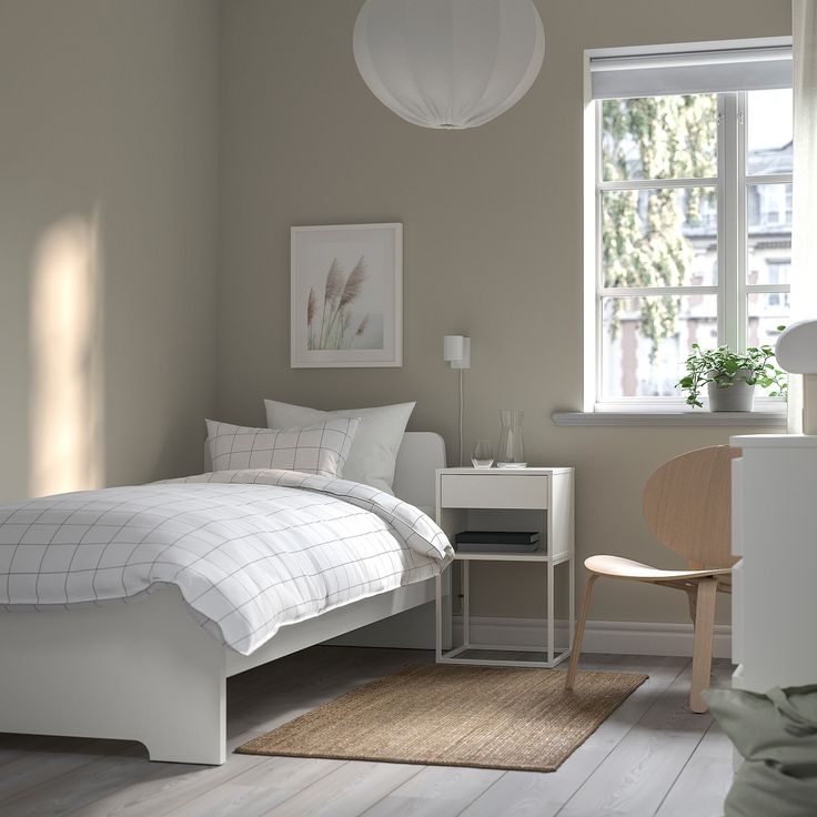 a white bed sitting next to a window on top of a wooden floor in a bedroom