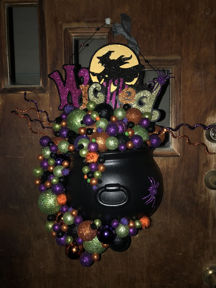 a witch's caulder is decorated with halloween balls and glitters on the front door