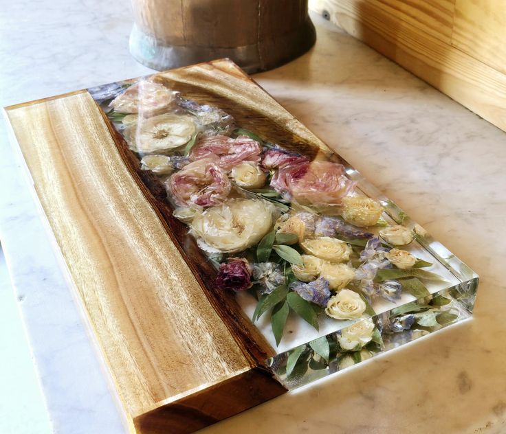 a wooden cutting board sitting on top of a counter next to a vase filled with flowers