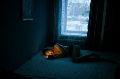 a woman laying on top of a bed in a dark room next to a window