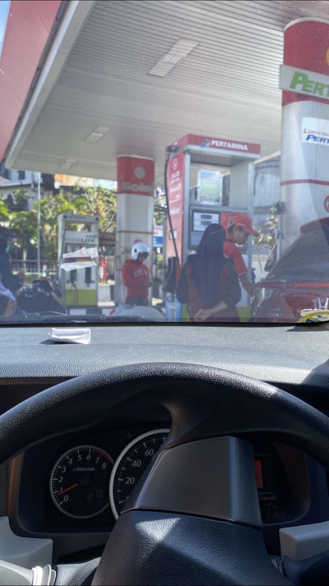 the dashboard of a car in front of a gas station with people standing around it