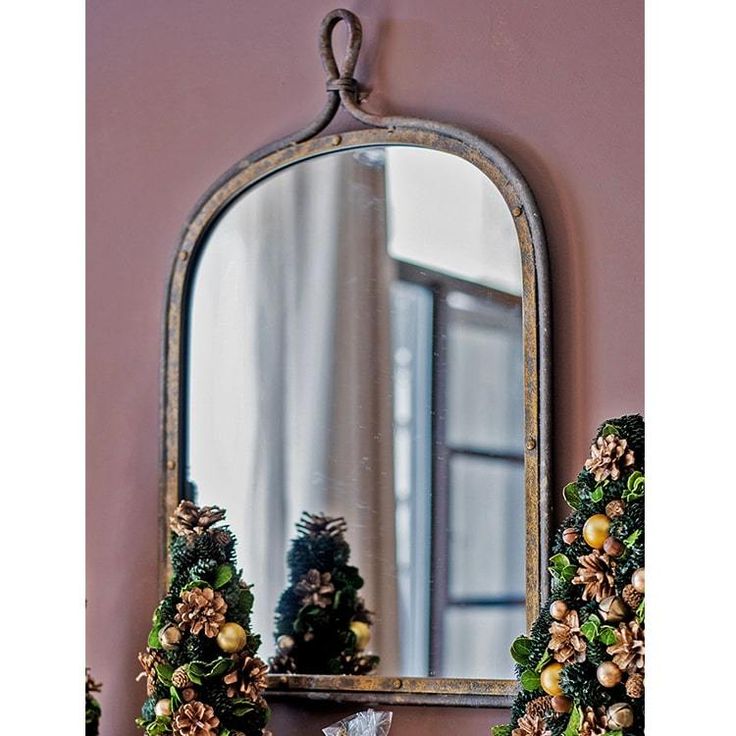 a mirror sitting on top of a mantle next to a vase filled with flowers and pine cones