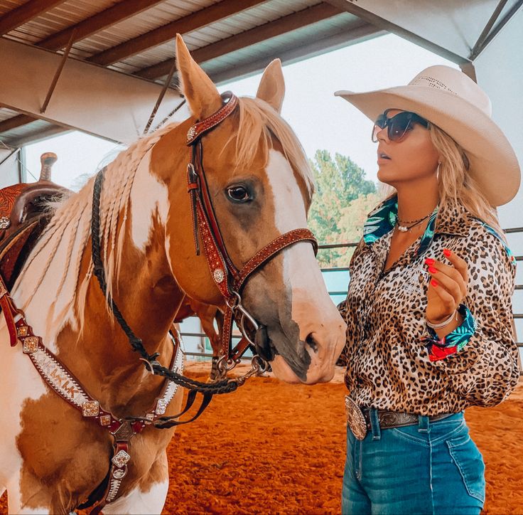 a woman standing next to a brown and white horse wearing a cowboy's hat