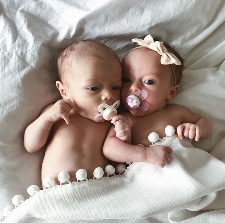 two babies laying on top of a bed with pacifiers in their mouths and noses