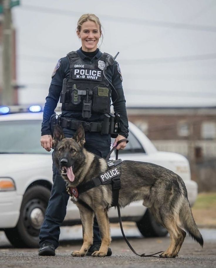 a woman police officer standing next to her german shepard dog on a leash in front of a police car