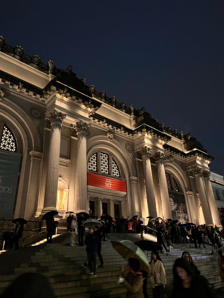 many people are walking up and down the stairs in front of a building at night