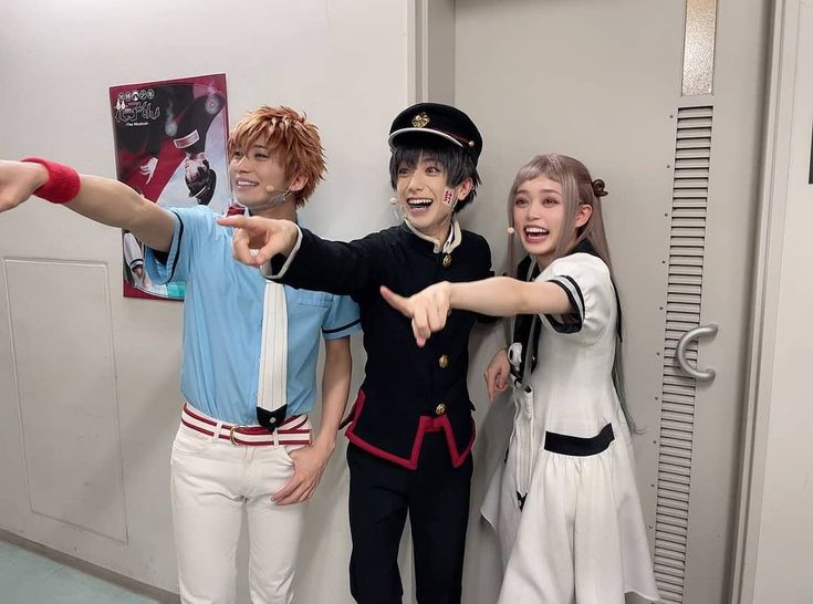 three young people dressed in costumes pointing at something with one hand and the other holding out his thumb