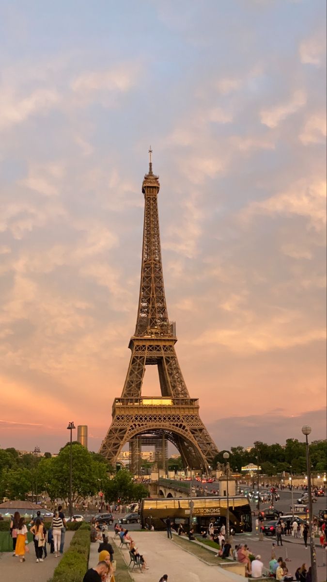 the eiffel tower in paris, france at sunset with people sitting and walking around