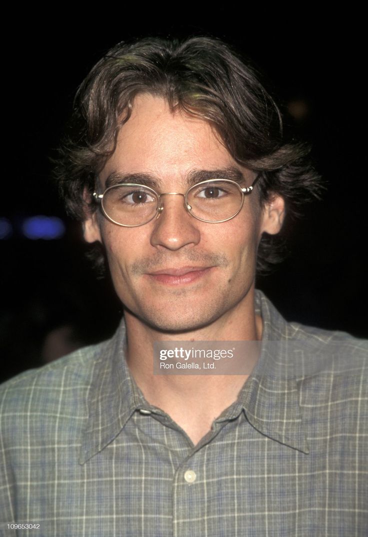 a man with glasses smiling at the camera in front of a dark background stock photo