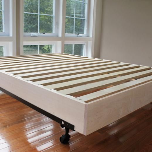 a bed frame sitting on top of a hard wood floor next to two large windows