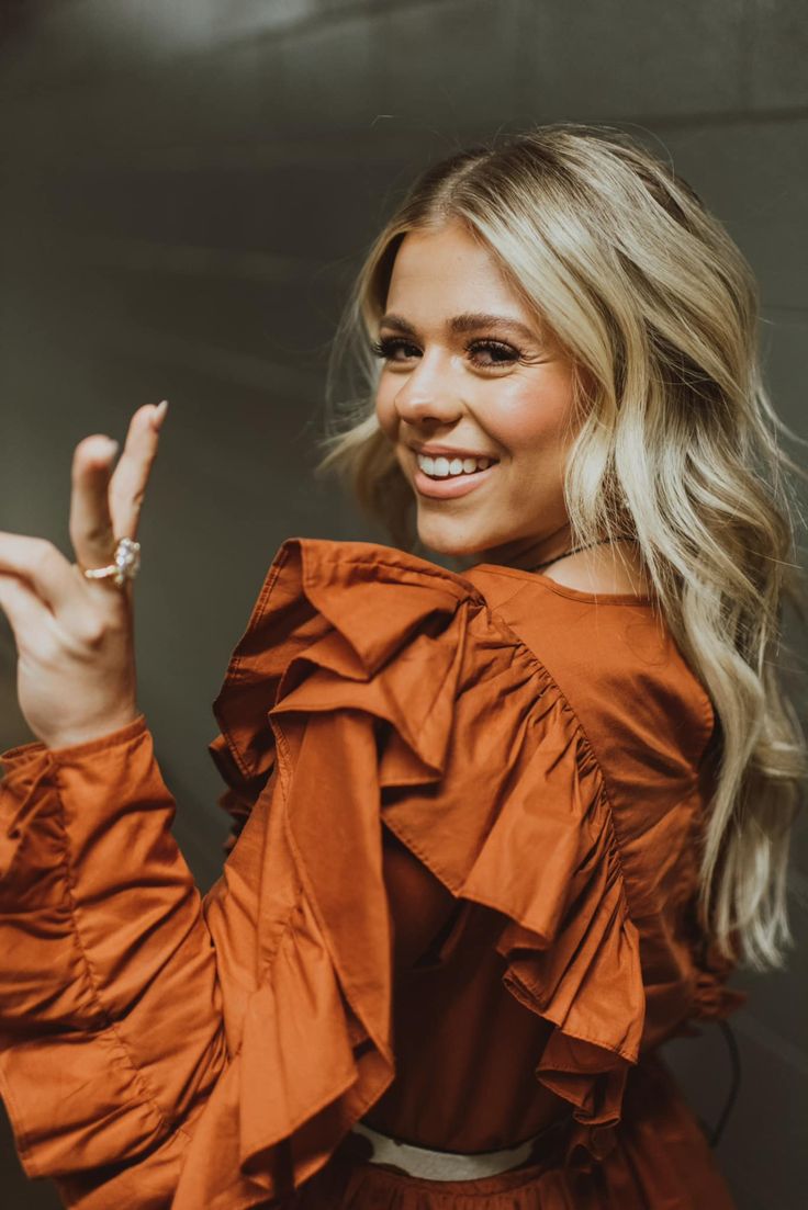 a woman in an orange top is smiling and holding her hand up