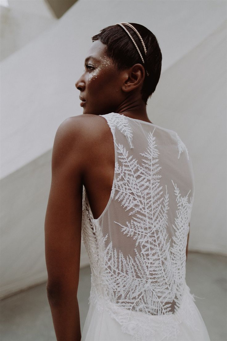 a woman wearing a white wedding dress standing in front of a wall and looking off into the distance