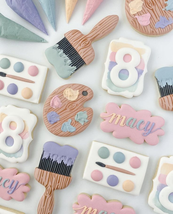 decorated cookies are arranged in the shape of brush, palettes and letters on a white surface