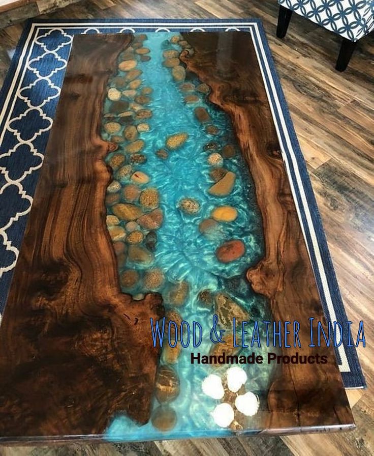 a coffee table with blue water and rocks in the middle on a wooden floor next to a chair