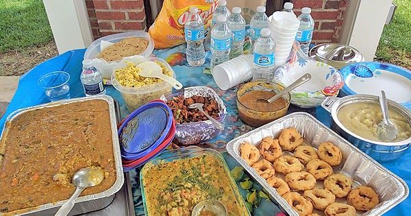 a table filled with lots of food on top of a blue cloth covered picnic table