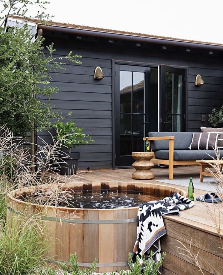 a wooden hot tub sitting in the middle of a garden next to a patio area