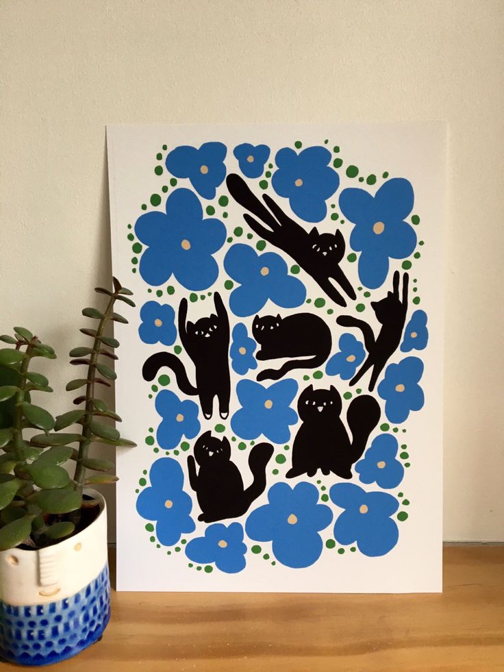 a blue and white card with black cats on it next to a potted plant